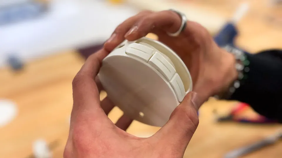 Two hands holding a white printed model of Senzu