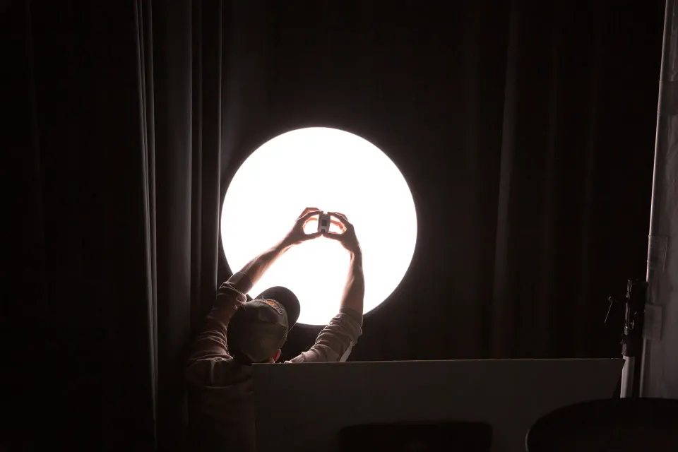 A person in a dark room forming a heart with their hands in front of a round light
