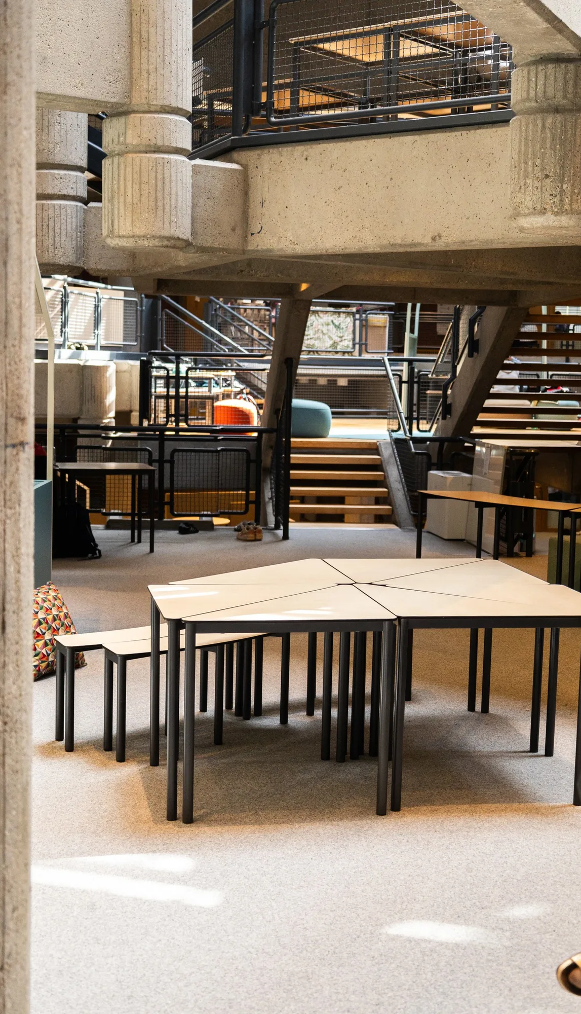 Group of trapezoid tables pushed together in the open area, stairs in the background