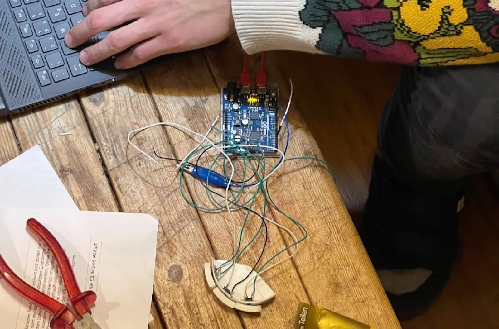 An Arduino board with jumper wires on a wooden table next to a laptop